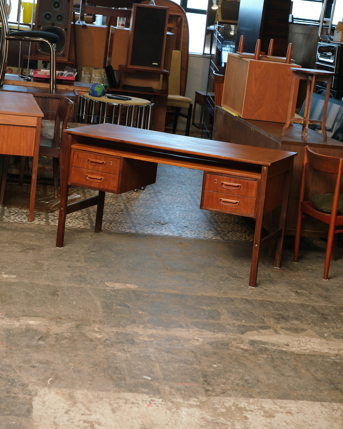 Mid-century modern teak desk shown from the front, with four drawers and a floating top over tapered splayed legs, among