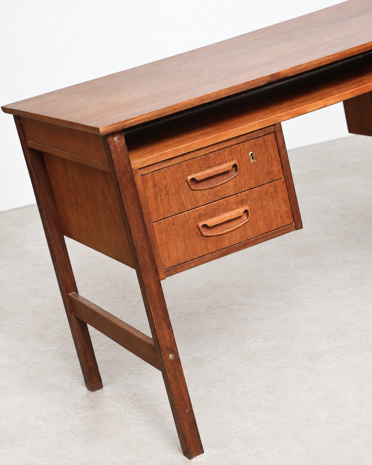 Close-up of the desk's drawer bank, brass keyhole, and sculpted teak pulls, with tapered leg visible.
