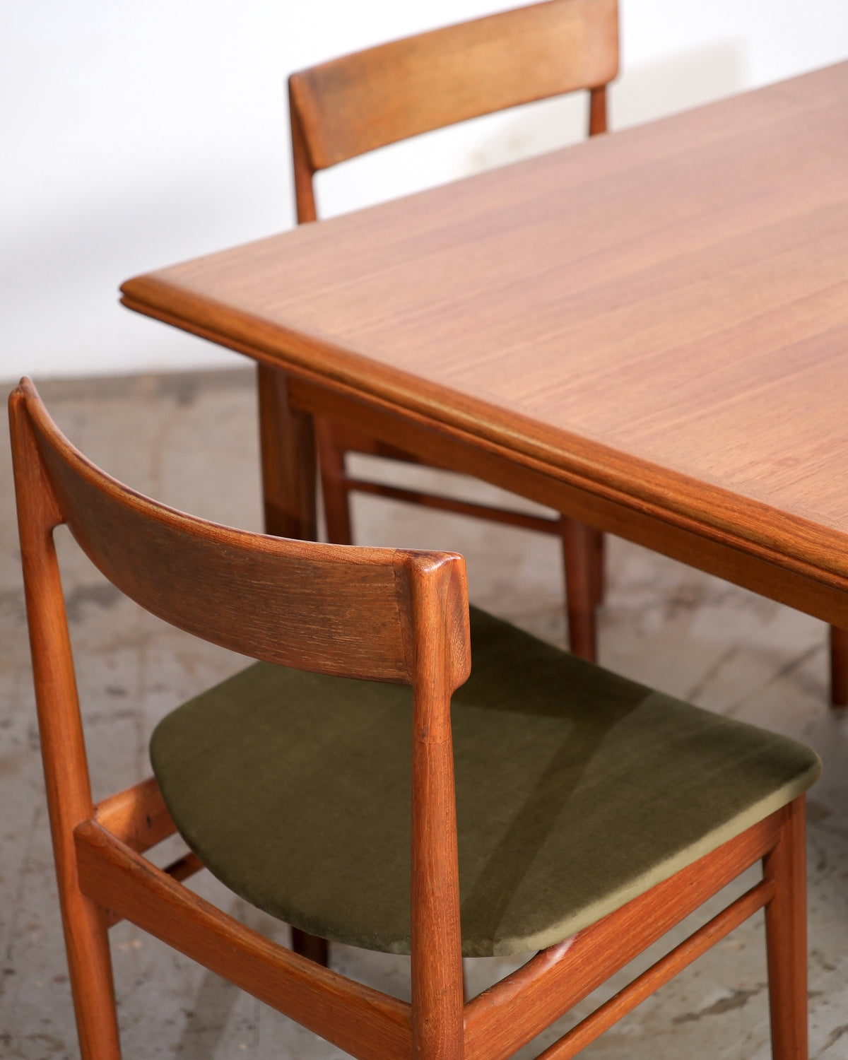 Close-up of two teak dining chairs and table edge showing grain and joinery