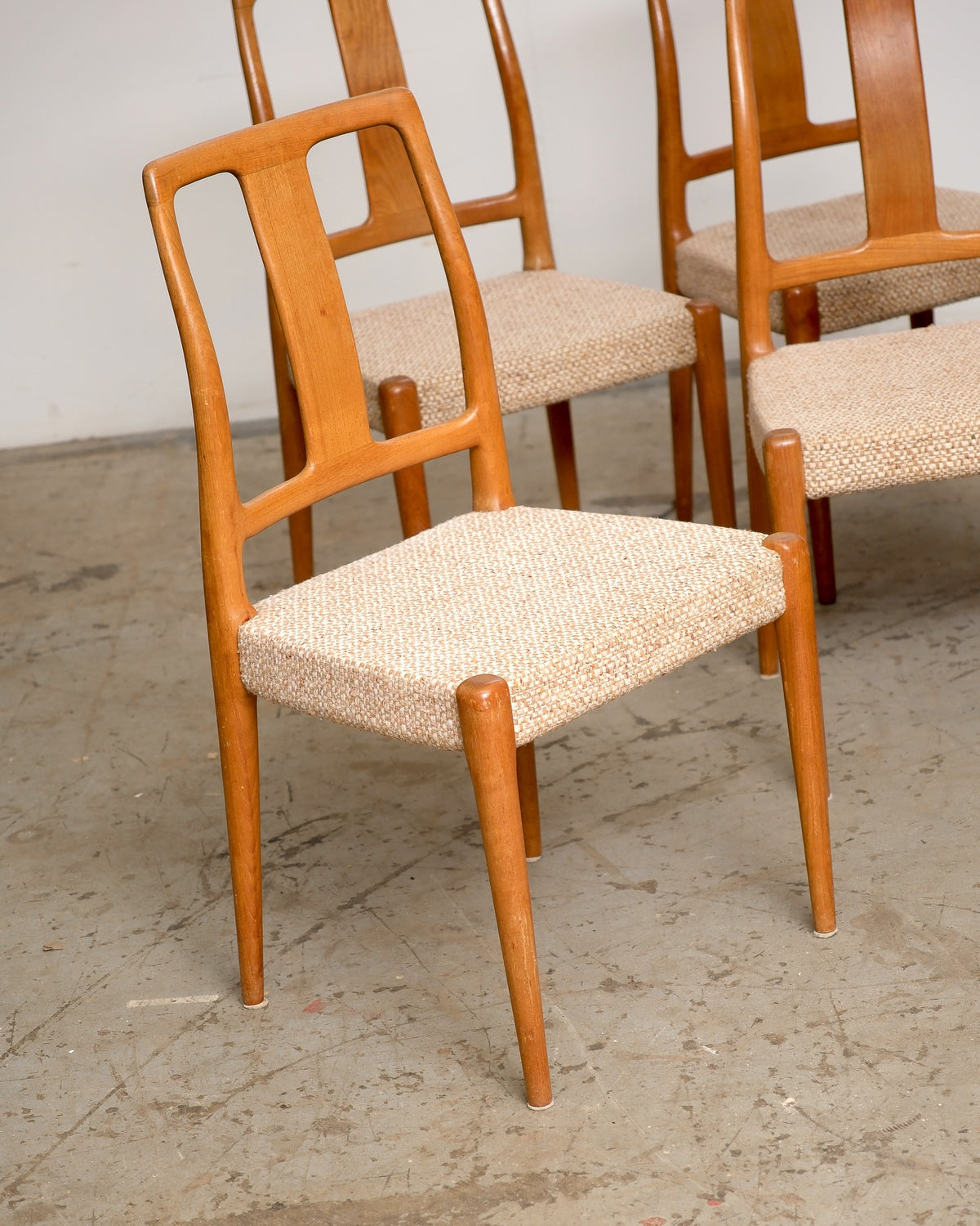 Side view of a dining chair showing its sculpted backrest and tapered teak legs