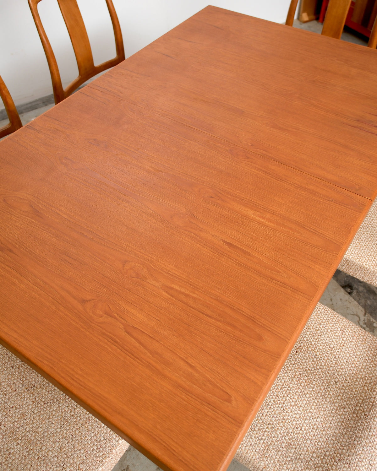 Close-up of the teak dining table surface showing the natural wood grain and leaf seam