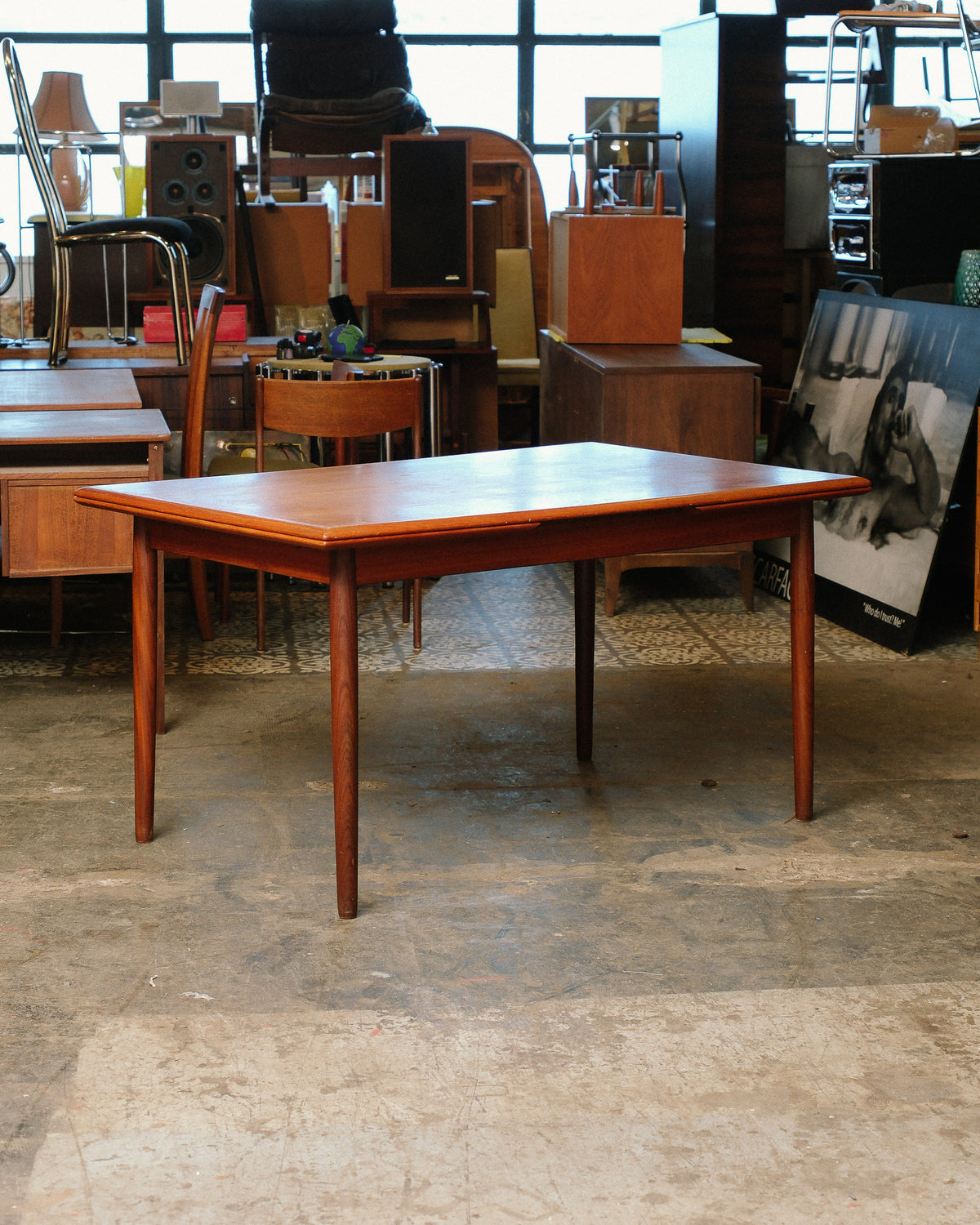 Front view of the teak dining table fully assembled on tapered round legs in a showroom.