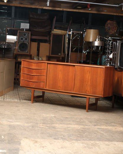 Full side view of the teak sideboard in a warehouse setting, showing drawers and sliding doors.
