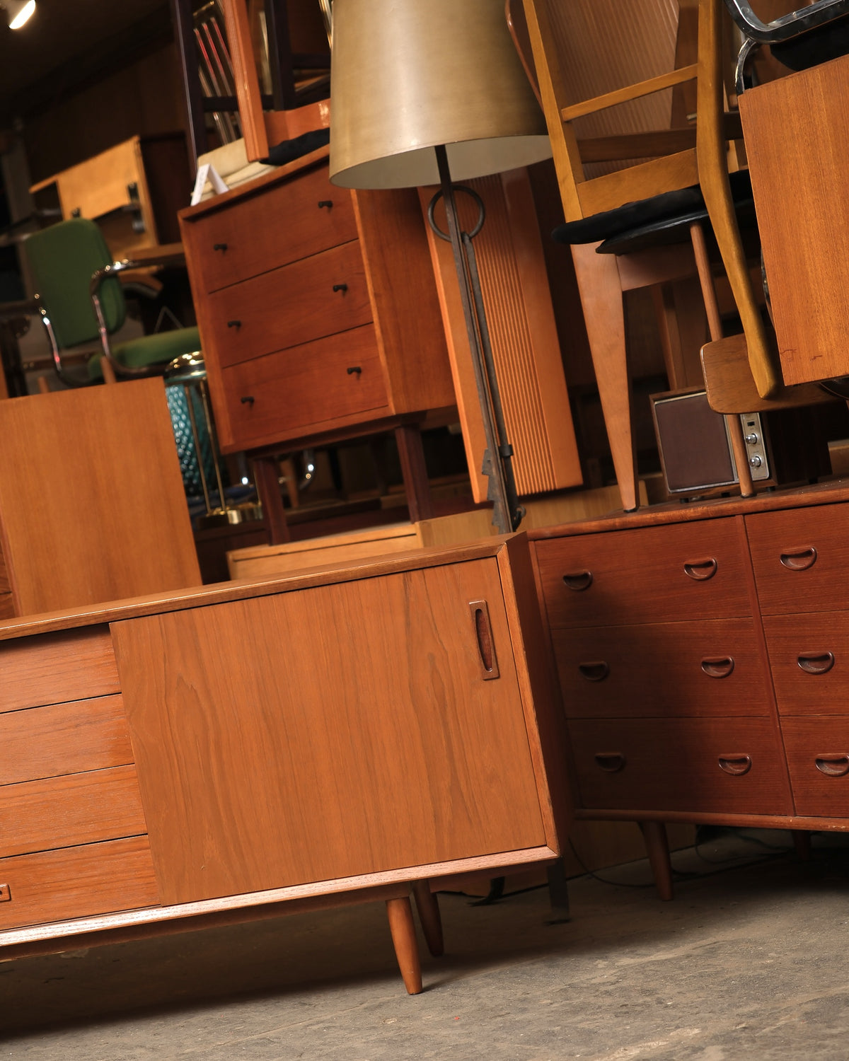 Side angle of the sideboard among other vintage teak furniture in the warehouse