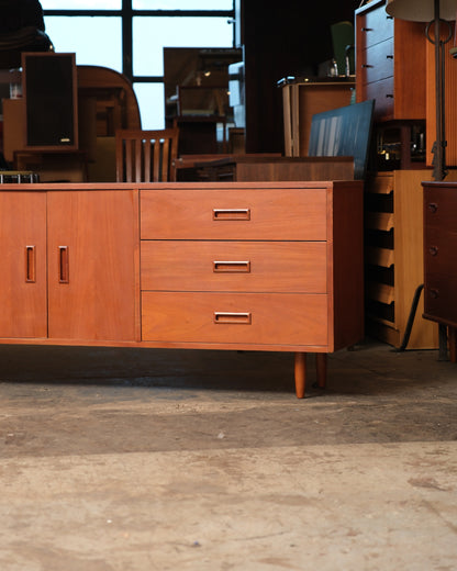 Angled view of a mid-century modern teak wide sideboard with drawers and a two-door cabinet, shown in a vintage furniture