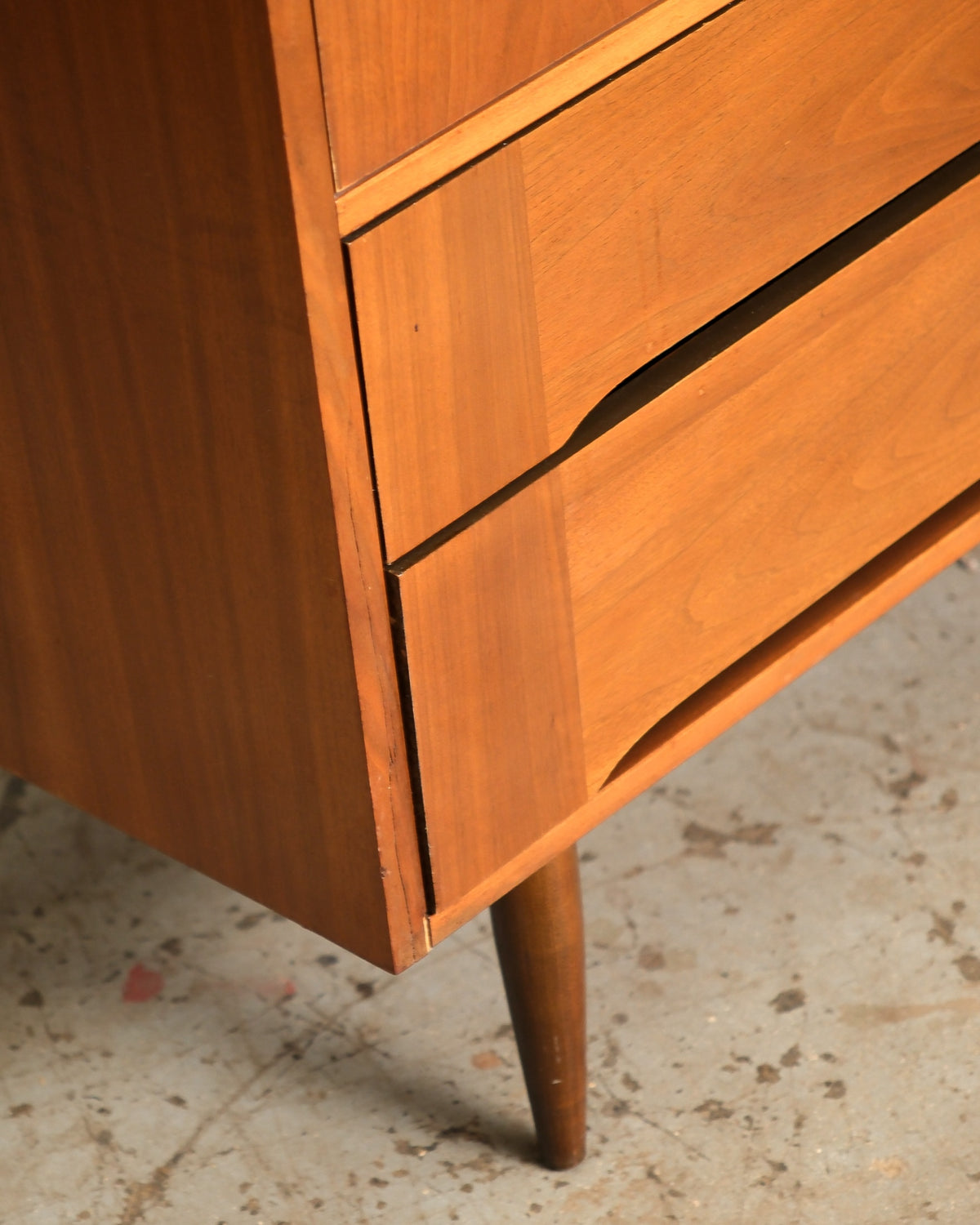 Close-up of the lower right corner showing tapered leg, drawer pull detail, and walnut grain.