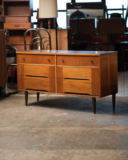 Front view of the dresser shown in a showroom setting with other vintage furniture nearby.