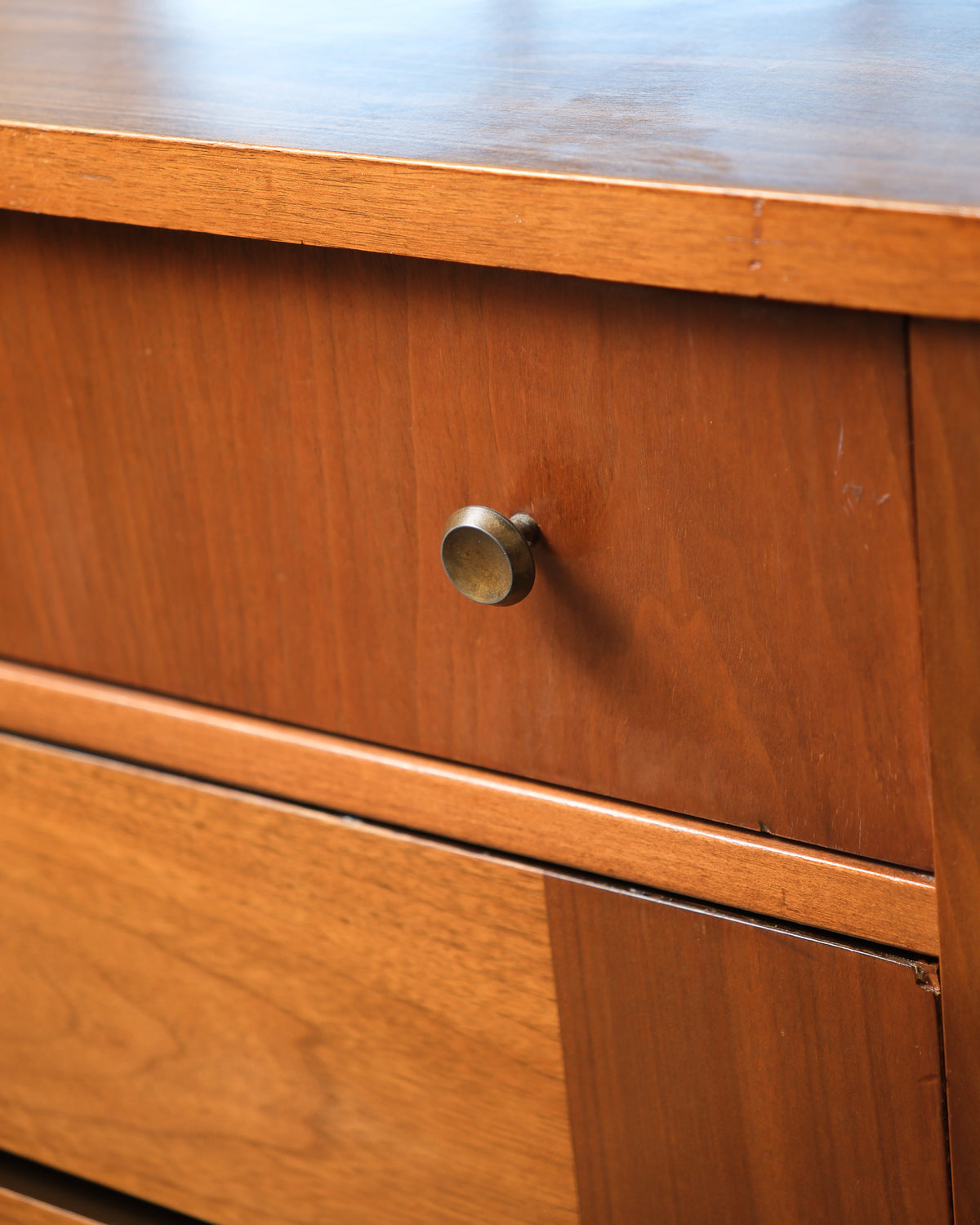 Close-up of a single brass drawer knob against the walnut drawer face.