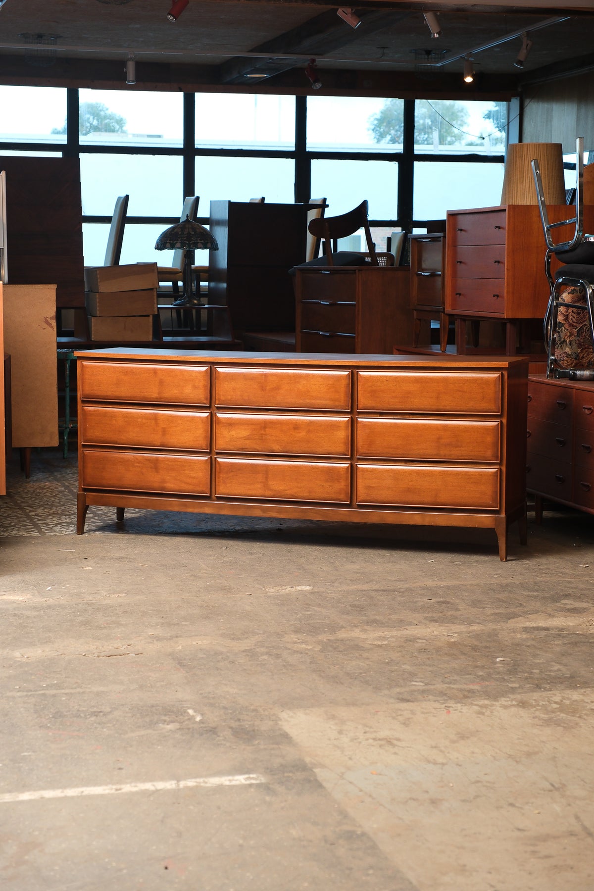 Front view of a mid-century walnut 9-drawer dresser with sculpted drawer fronts and tapered legs, shown in a furniture