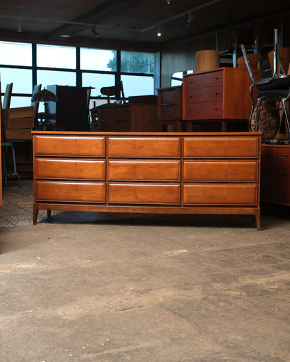Front view of the dresser against a showroom backdrop with other vintage furniture pieces visible.