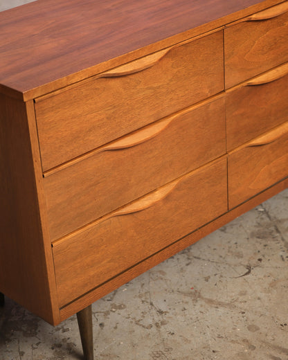 Close-up angle of a walnut 9-drawer dresser showing sculpted finger-pull handles and grain detail.