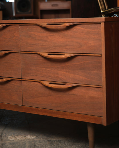 Close-up of three drawer fronts showing sculpted pull handles and walnut grain detail
