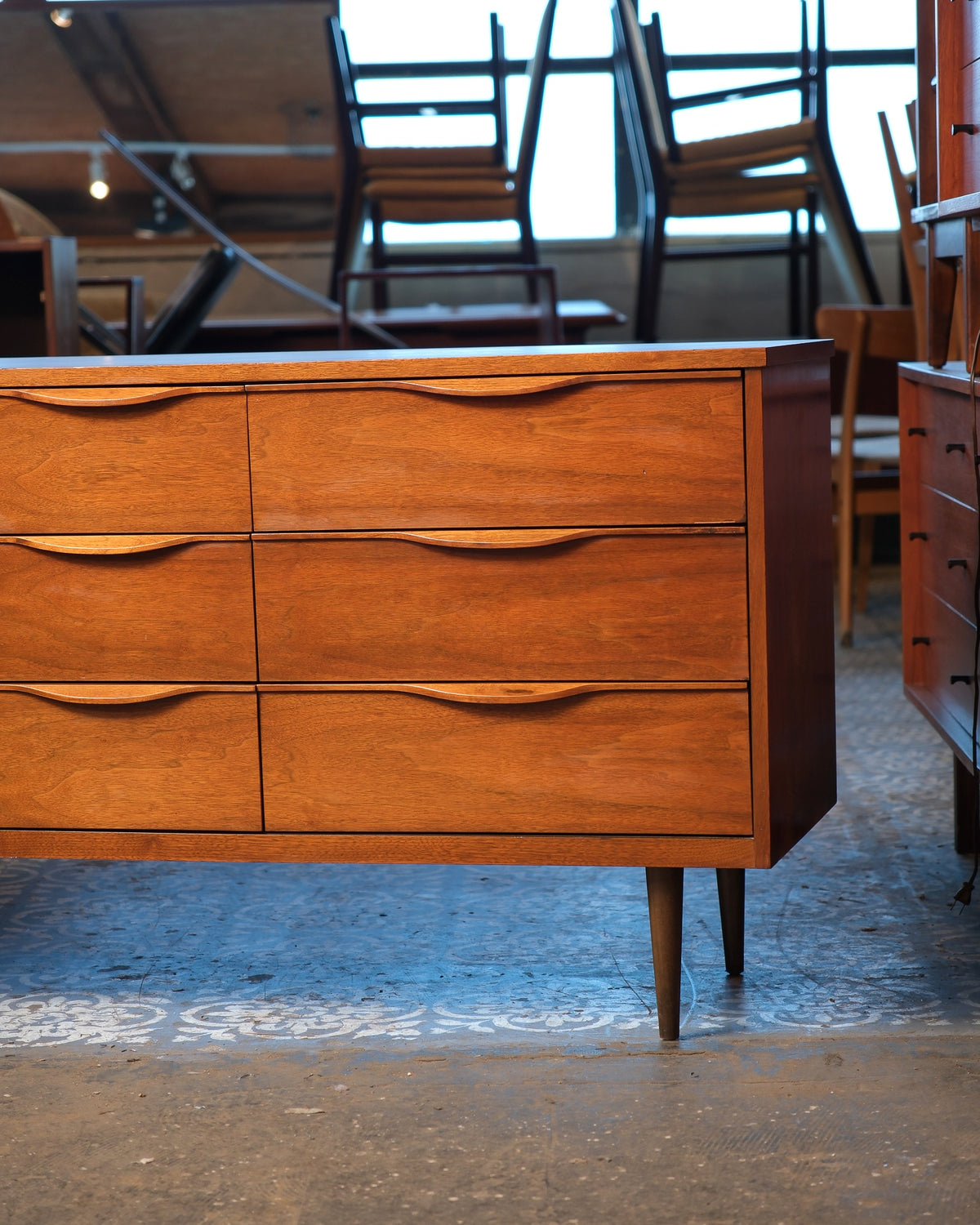 Side view of the walnut dresser showing all six front drawers and tapered legs, set in a furniture showroom.