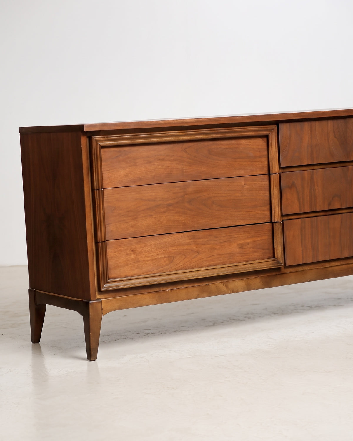 Front corner view of the dresser showing drawer banks, tapered leg, and hardware-free pulls.