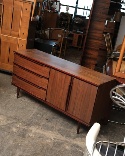 Front angle view of the walnut credenza with three drawers and two paneled cabinet doors closed