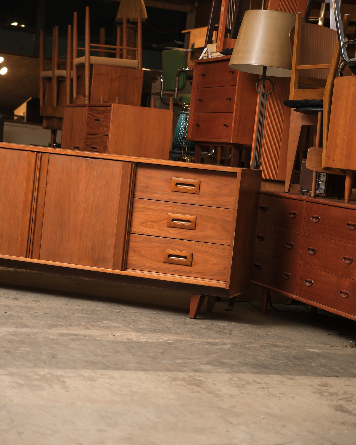 Angled view of the walnut sideboard with drawers and sliding doors, set against other mid-century furniture pieces.