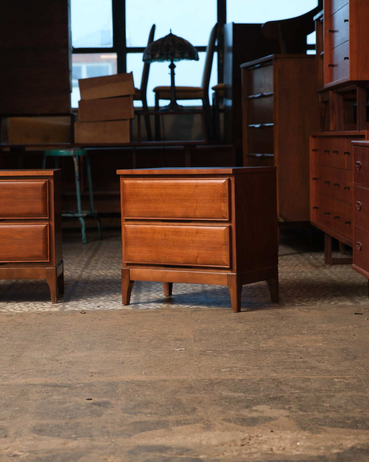 Front view of one walnut nightstand with two drawers, shown in a furniture showroom setting.