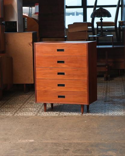 Mid-century teak tallboy dresser with five drawers and recessed black pulls, shown straight on in a showroom setting.