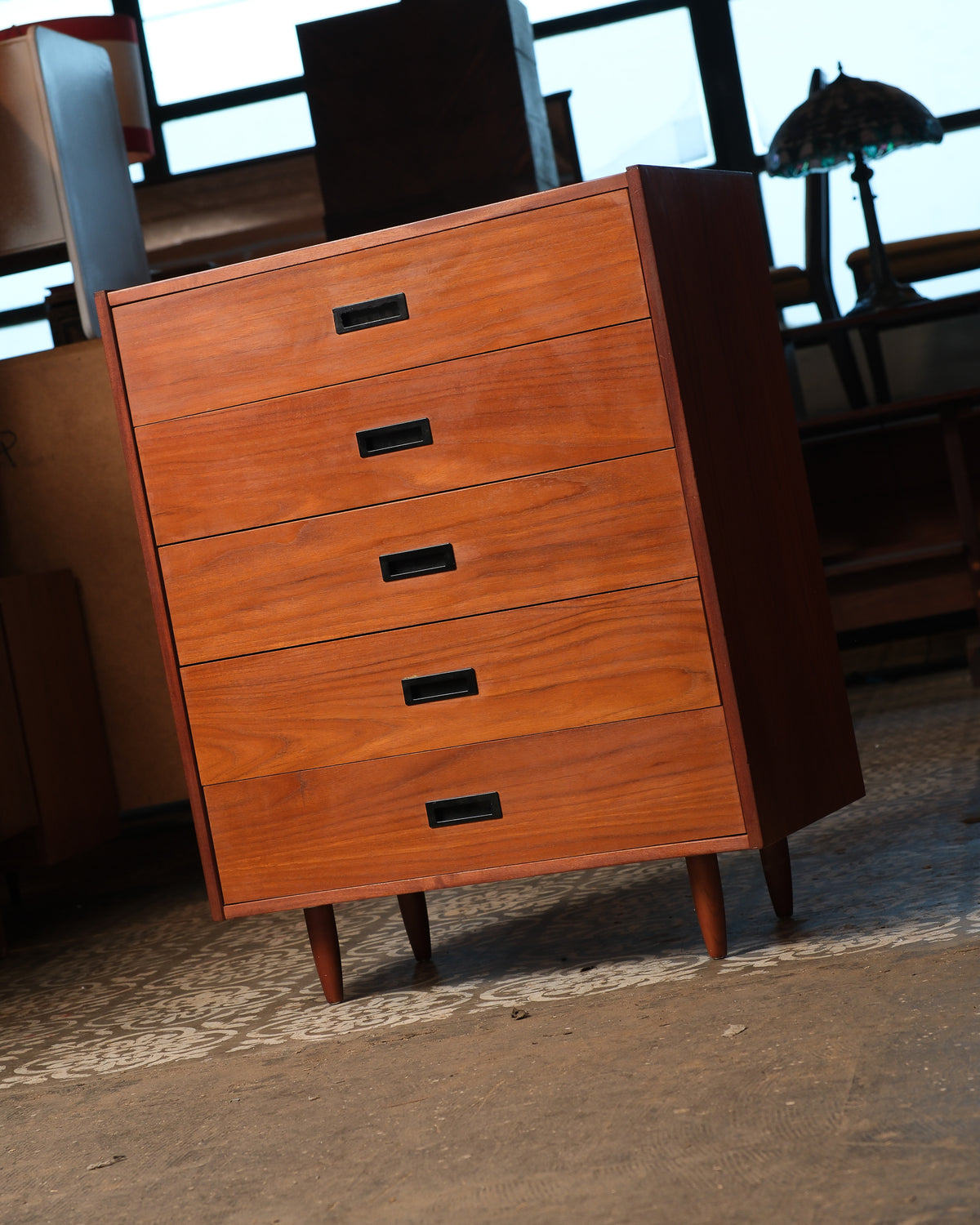 Angled view of the teak tallboy dresser showing tapered legs and side profile.