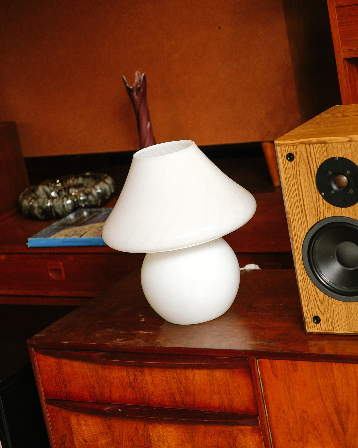 White Murano mushroom opaline glass table lamp displayed on a teak sideboard beside a wooden speaker.
