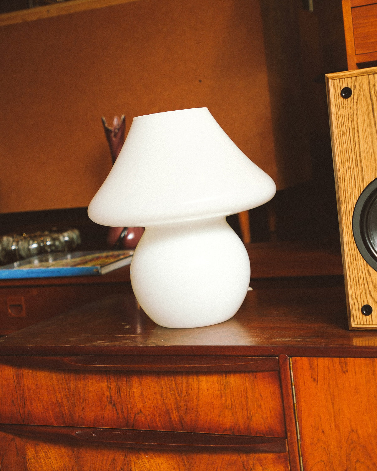 Side view of the opaline glass mushroom lamp showing its rounded base and wide shade on a wood cabinet.