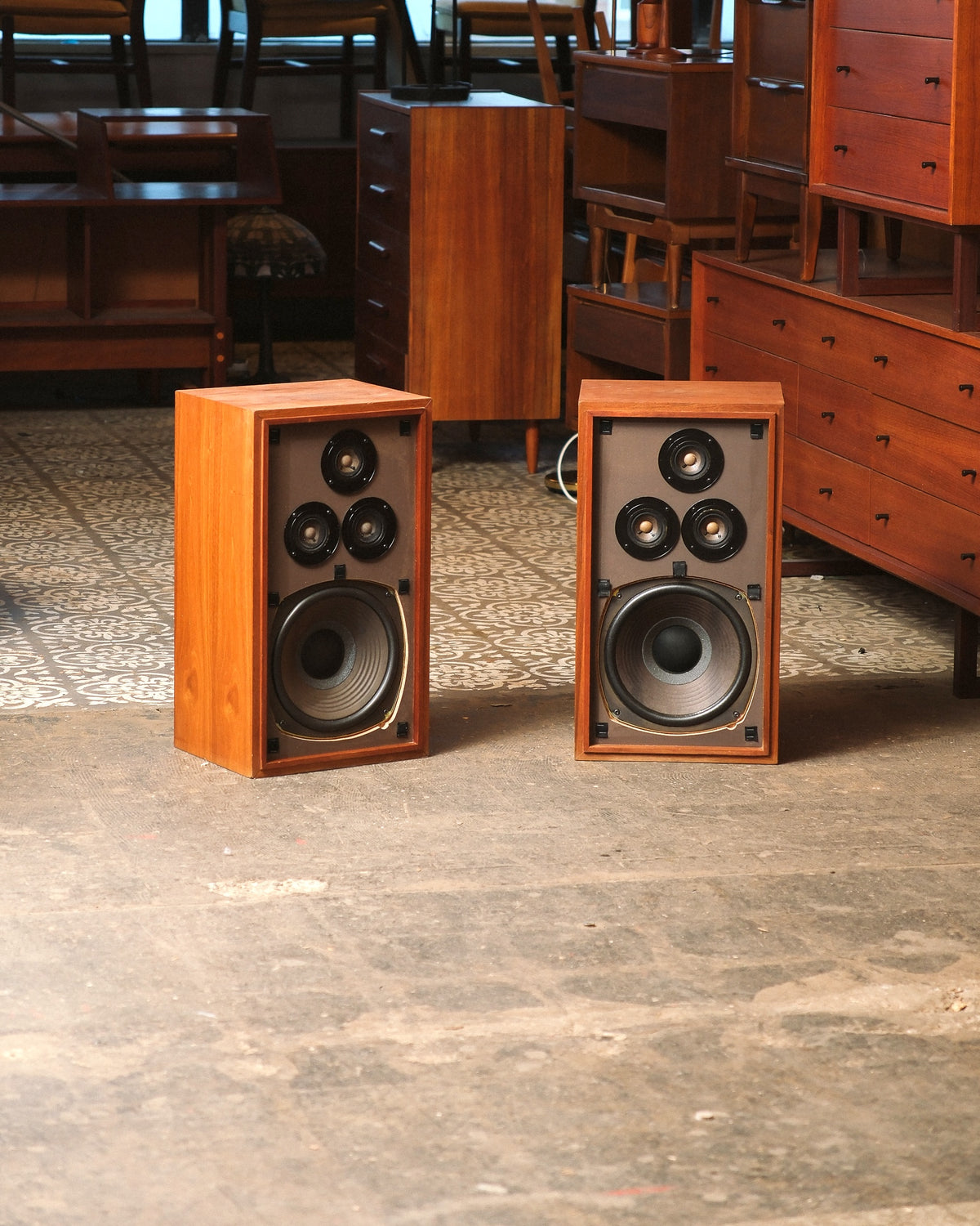 Pair of vintage Realistic walnut speakers with grilles removed, shown among mid-century furniture in the showroom.