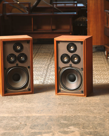 Front view of the walnut speaker pair with grilles off, showing tweeters and woofers side by side.