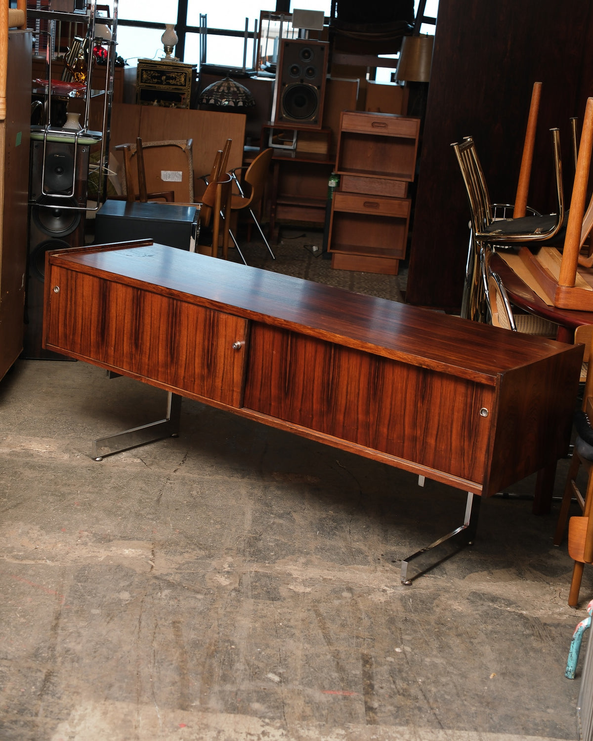 Angled view of a rosewood credenza with chrome legs, showing sliding doors and warm grain pattern