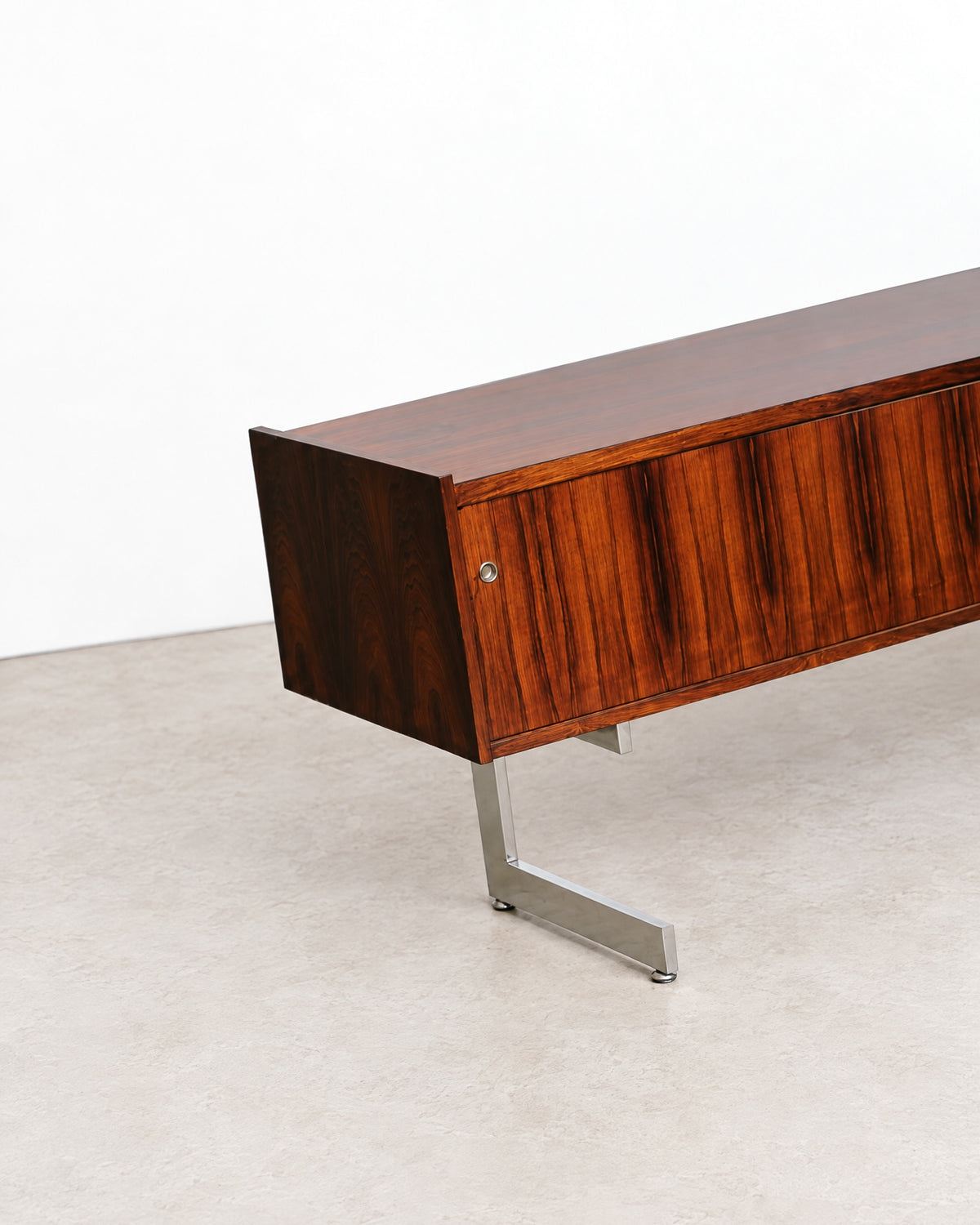 Front view of the rosewood credenza with sliding doors closed, set among other vintage pieces