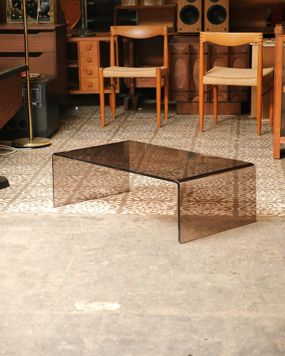Full view of the smoked lucite waterfall coffee table on a patterned floor, shown with other vintage furniture in the