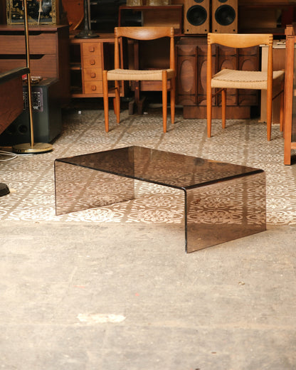 Full view of the smoked lucite waterfall coffee table on a patterned floor, shown with other vintage furniture in the
