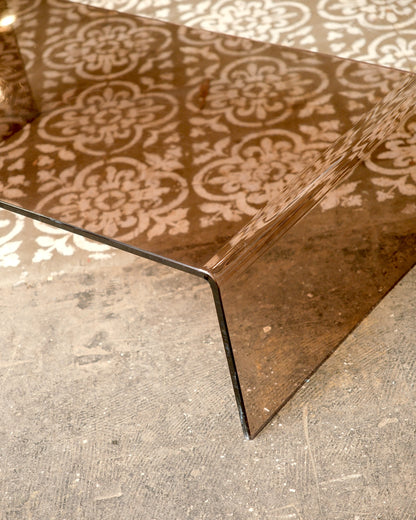 Angled close-up of the tabletop corner showing the curved waterfall edge and floor pattern reflected through the glass.