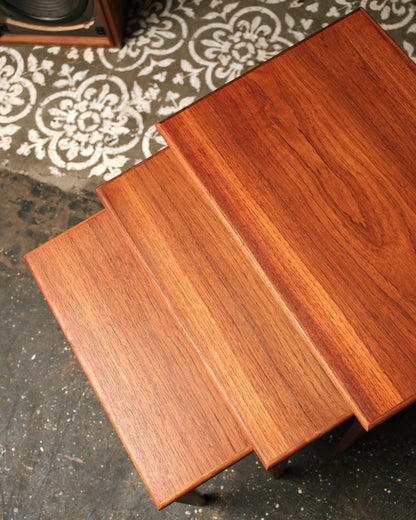 Overhead view of all three nesting tables stacked showing graduated sizes and teak grain