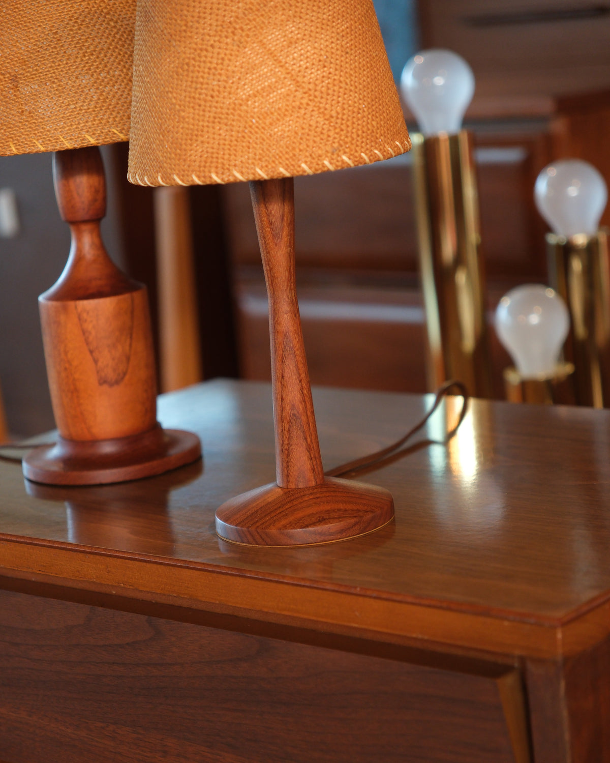 Detail view of the teak lamp's sculpted base beside another wooden lamp base on a wood surface.