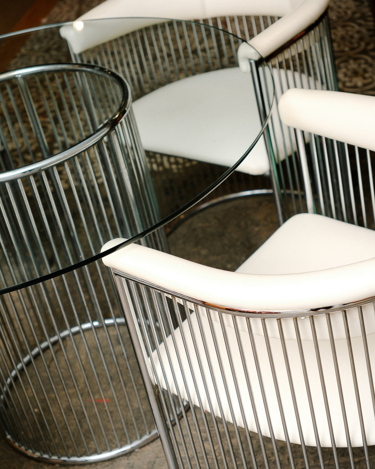 Close-up of two barrel-back chairs and the glass table edge, showing chrome and leatherette detail.