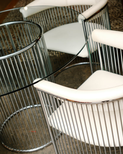 Close-up of two barrel-back chairs and the glass table edge, showing chrome and leatherette detail.