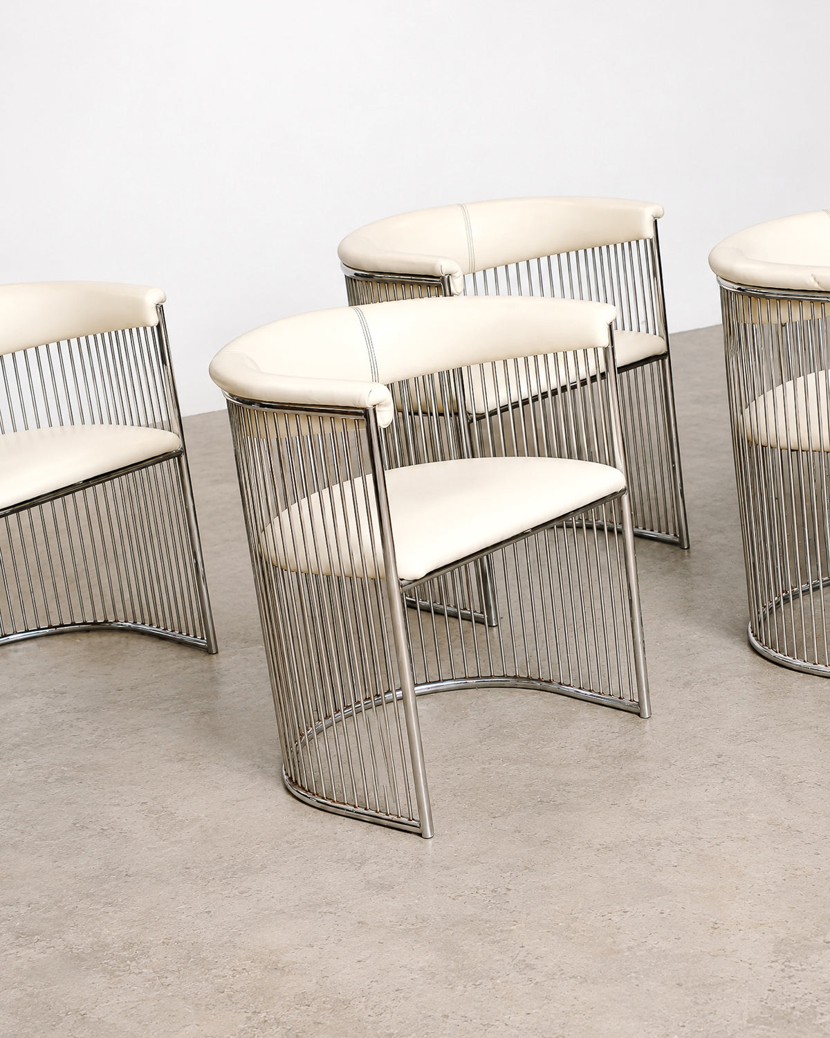 Detail of a chair's curved chrome armrest and cream leatherette seat.