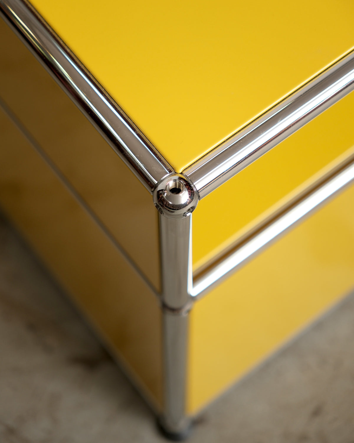 Close-up of the chrome ball joint corner on the USM Haller side table in golden yellow.