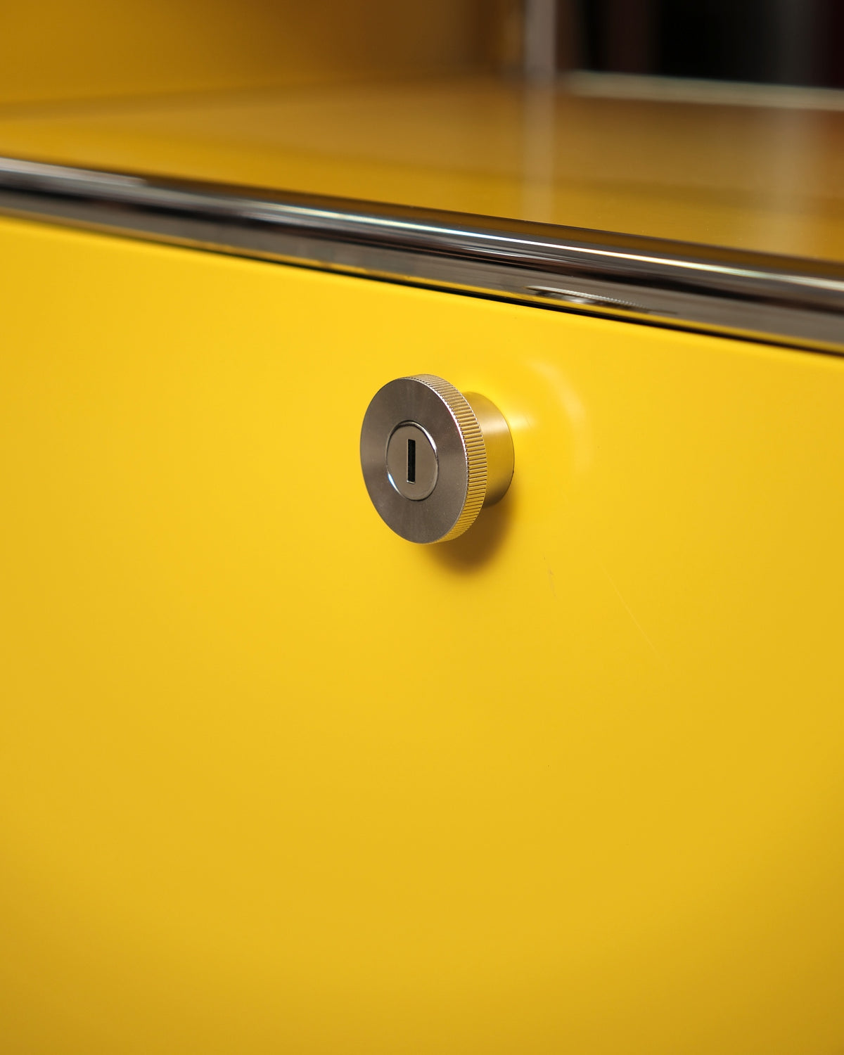 Detail of the round chrome key lock on the yellow cabinet door.