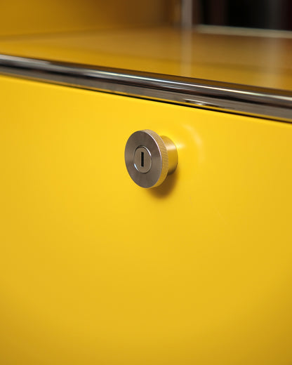 Detail of the round chrome key lock on the yellow cabinet door.