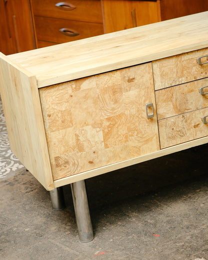 Angled view of the sideboard corner showing burl panels, drawer bank, and chrome leg.