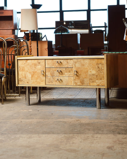 Front view of the burlwood sideboard shown on the showroom floor with chrome legs visible.
