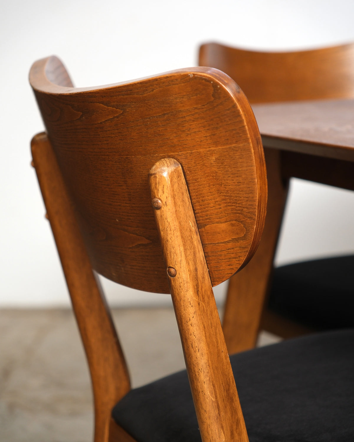 Close-up of a chair back showing curved crest rail joinery and wood grain, with the table behind.