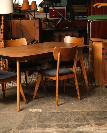 Full view of the oak dining table with four chairs set around it in a showroom setting.
