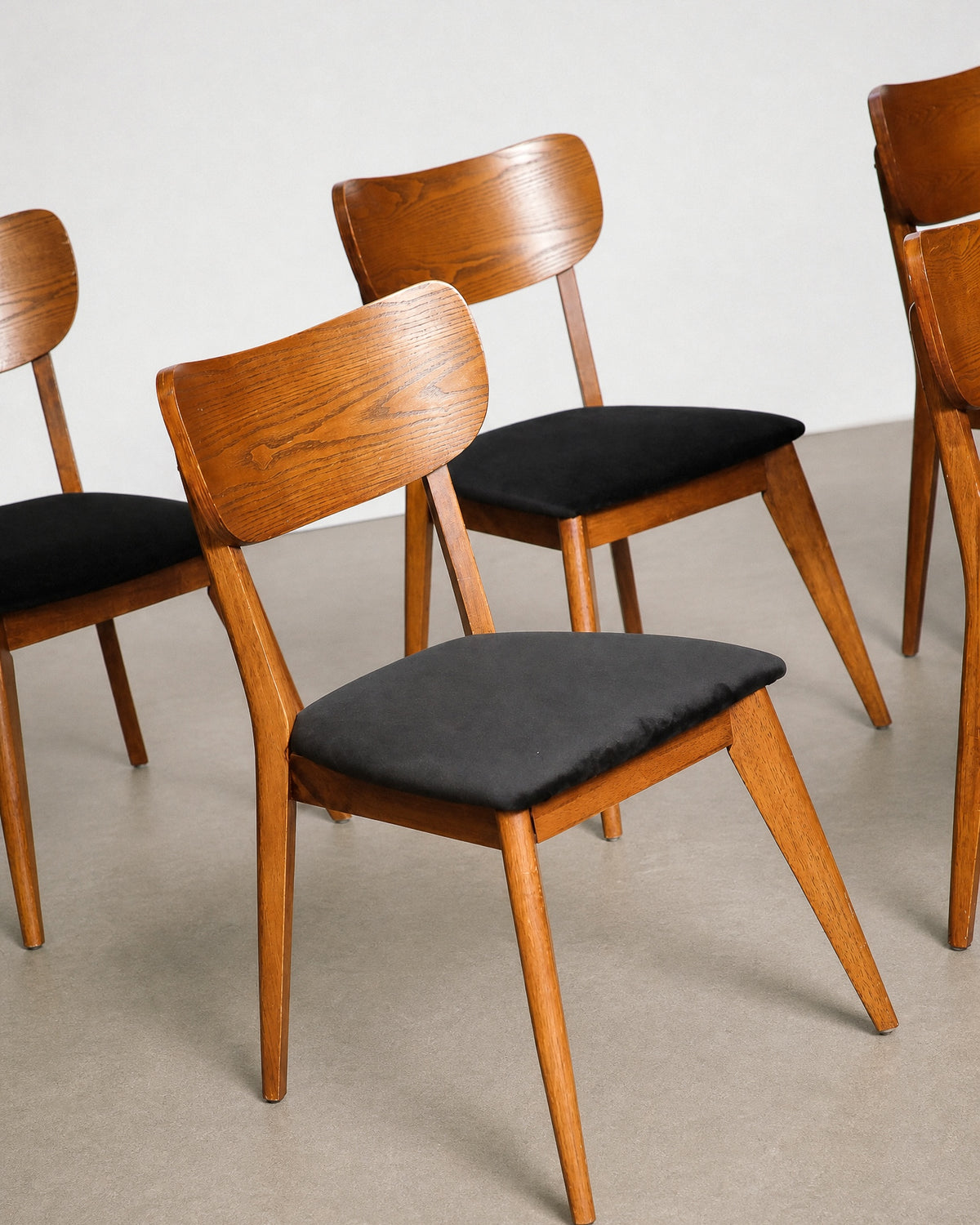 Close-up of two chairs showing the curved backrest, seat upholstery, and leg taper.