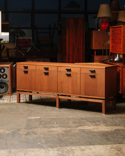 Vintage oak sideboard with four drawers and four cabinet doors, shown against a warehouse backdrop of other vintage pieces.