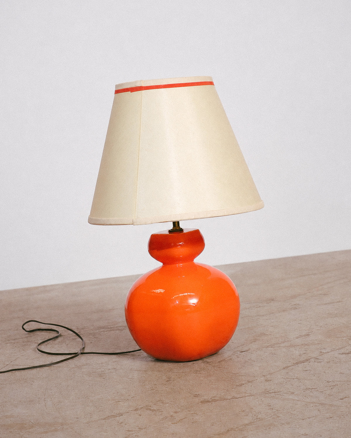Orange bulbous ceramic table lamp with cream shade and orange stripe, shown against a plain background.