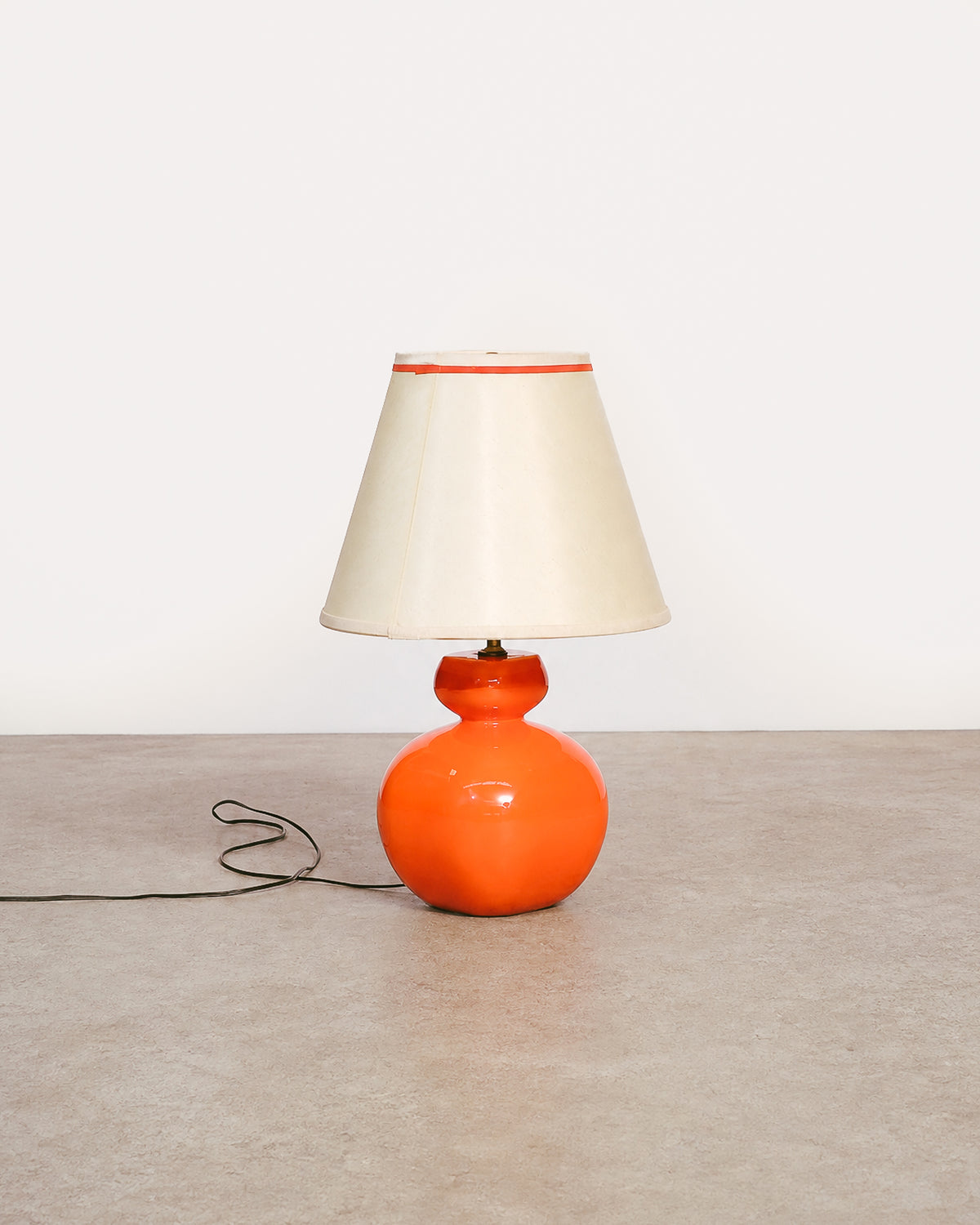 Front view of orange ceramic table lamp with cream lampshade on a bare floor.