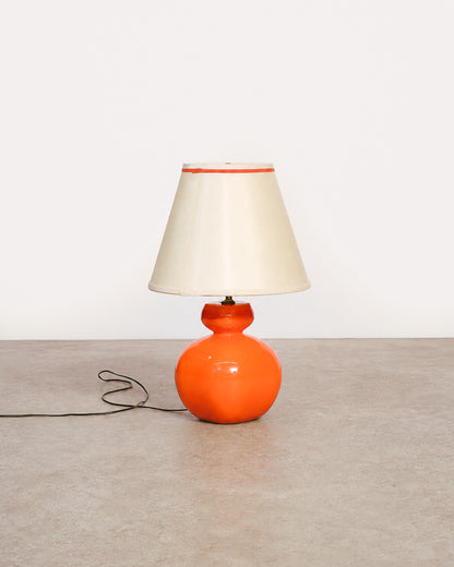 Front view of orange ceramic table lamp with cream lampshade on a bare floor.