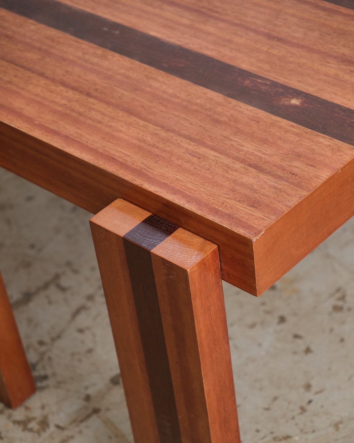Close-up of the tabletop corner showing contrasting wood stripe inlay and leg joinery.